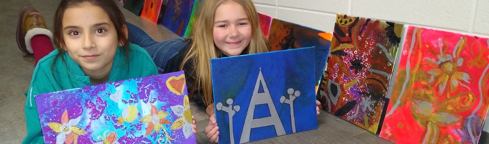 2 smiling students in Art Club displaying their art projects.